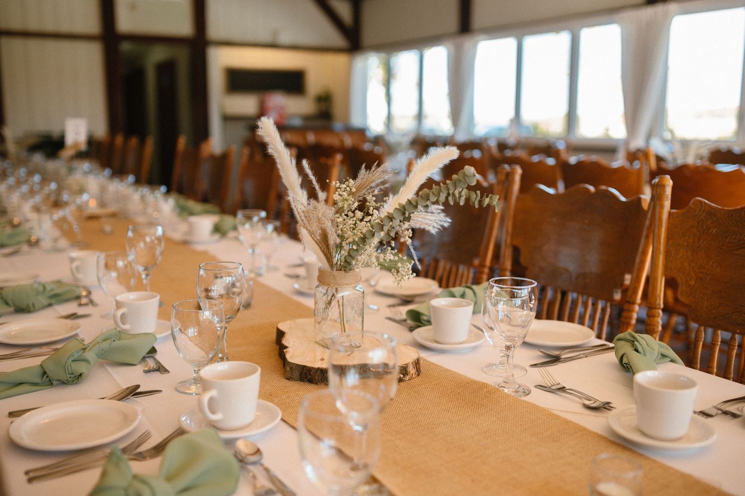 Elegant wedding reception table set with burlap runner, sage napkins, and floral centerpieces.