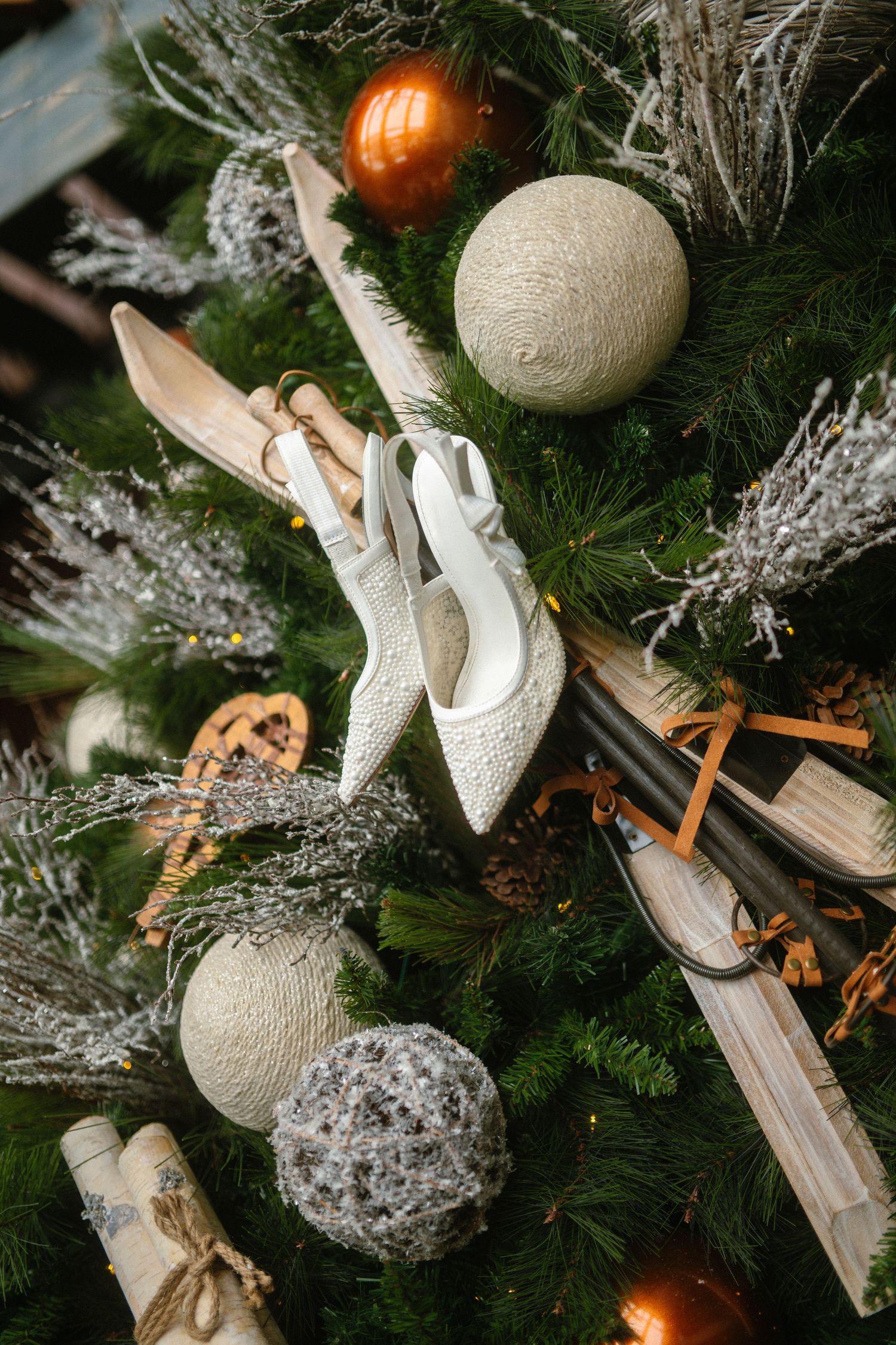White bridal heels displayed on a festive Christmas tree with ornaments, mini skis, and pine branches.
