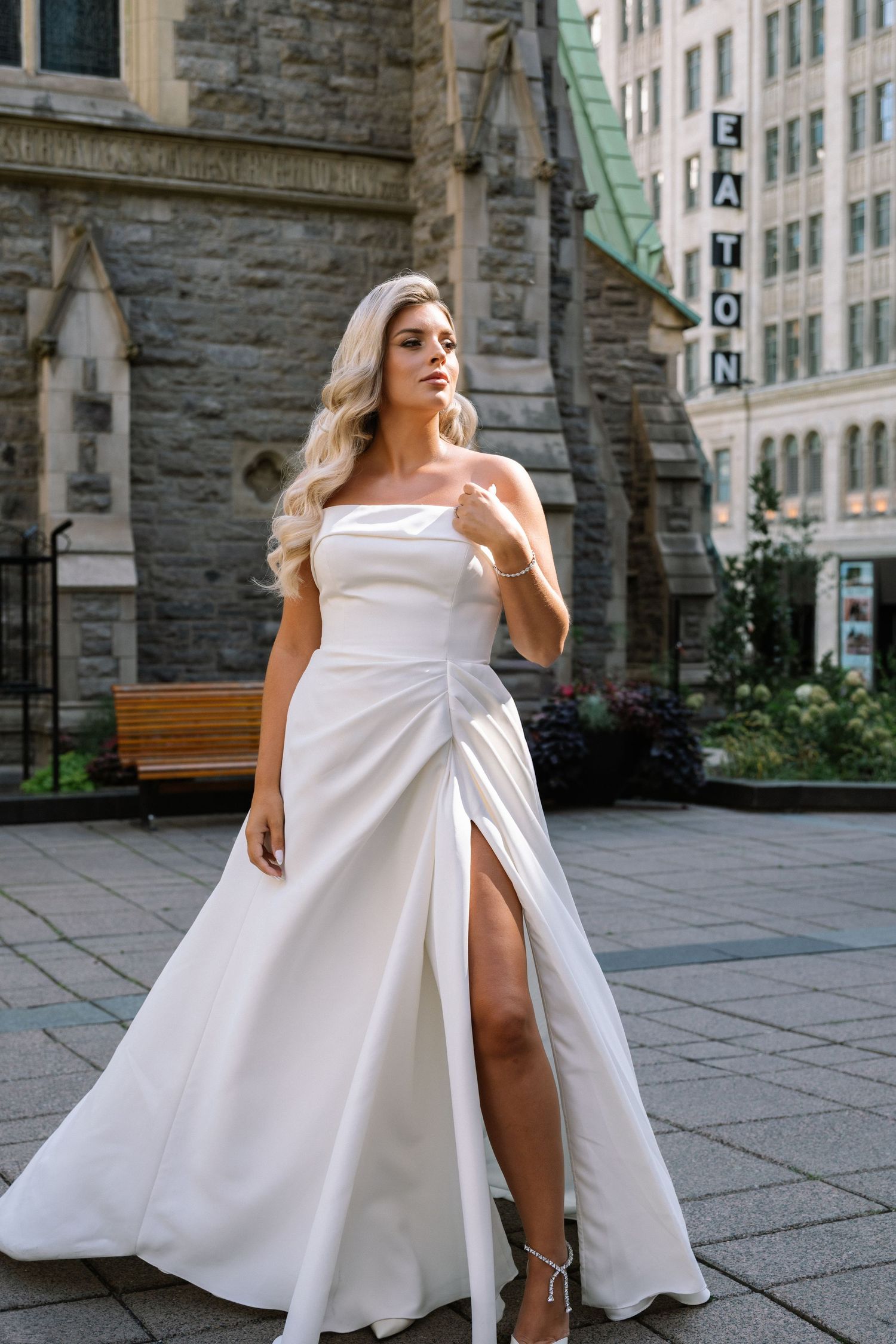 Elegant bride in a strapless white gown with a slit posing in an urban setting.