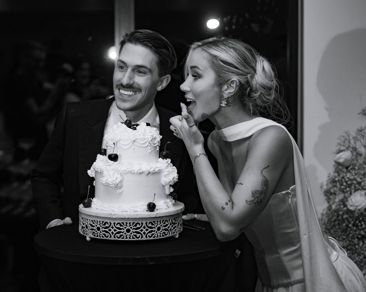 Black and white photo of a bride and groom smiling and cutting their white floral wedding cake.
