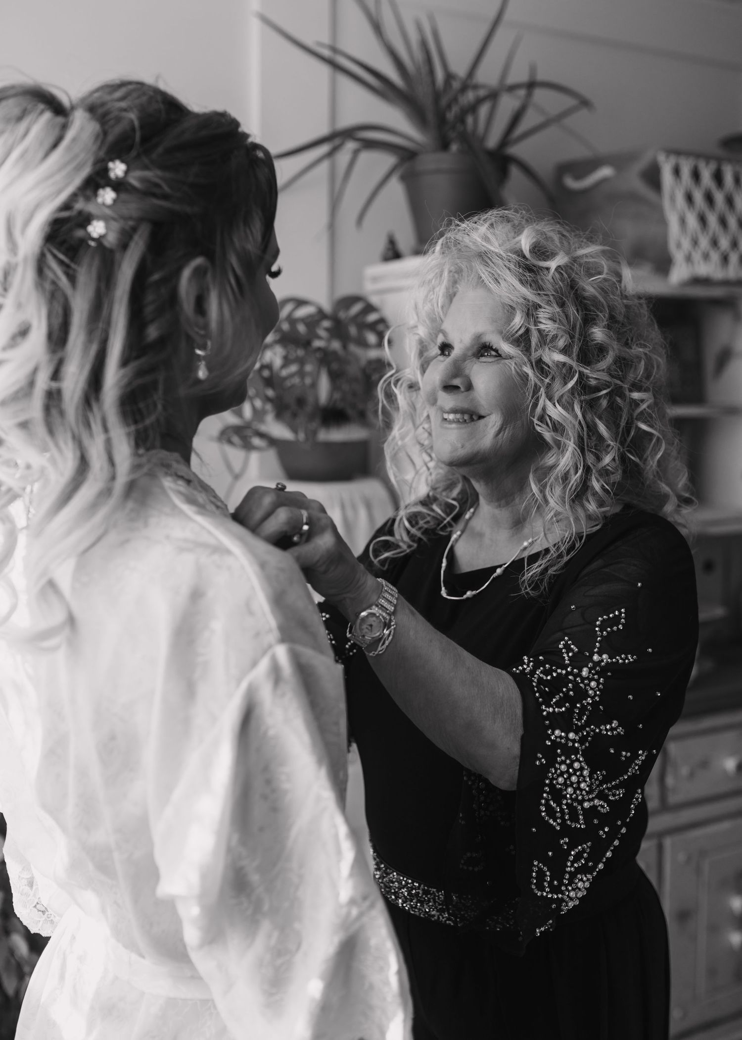 Black and white photo of a curly-haired woman helping a bride get ready on her wedding day.