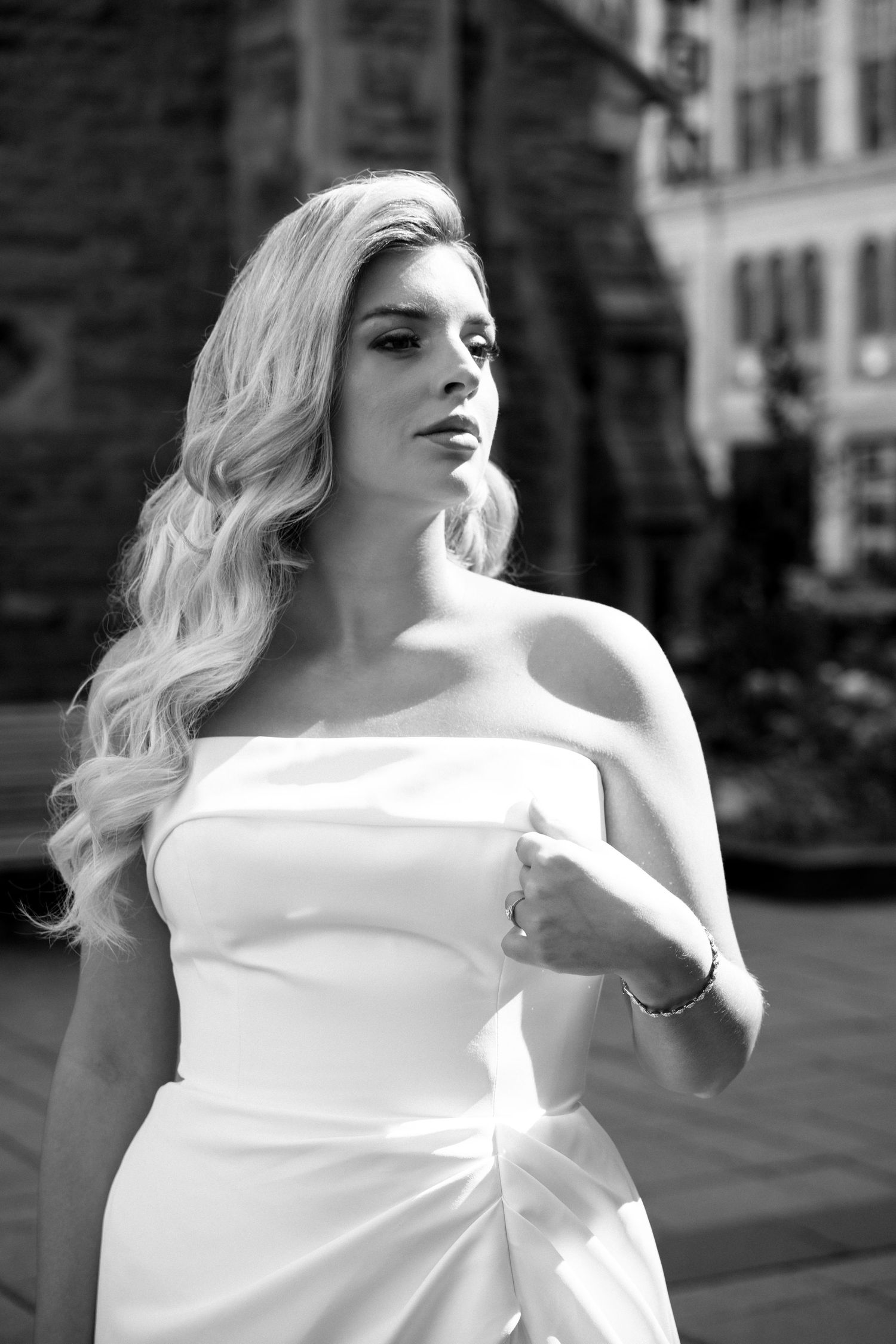 Elegant bride in strapless white gown with long blonde wavy hair posing outdoors in black and white photo.