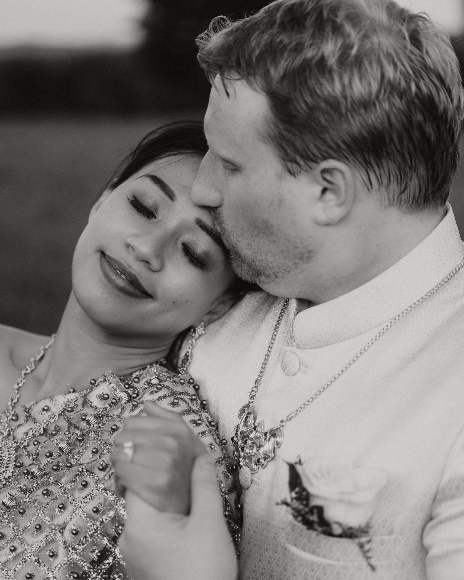 Black and white photo of a couple sharing a romantic kiss, woman in beaded dress smiling softly.