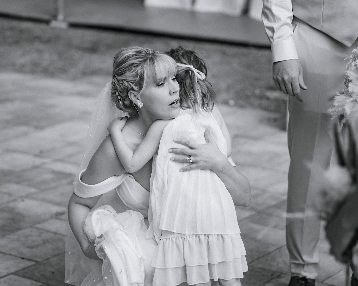 Two young flower girls share a sweet hug during a wedding ceremony in black and white photo.