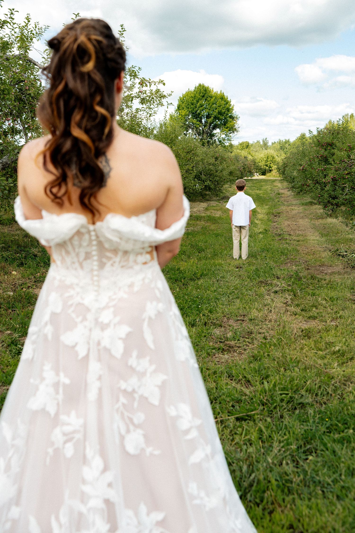 Bride in lace wedding gown facing a young boy in a garden path.