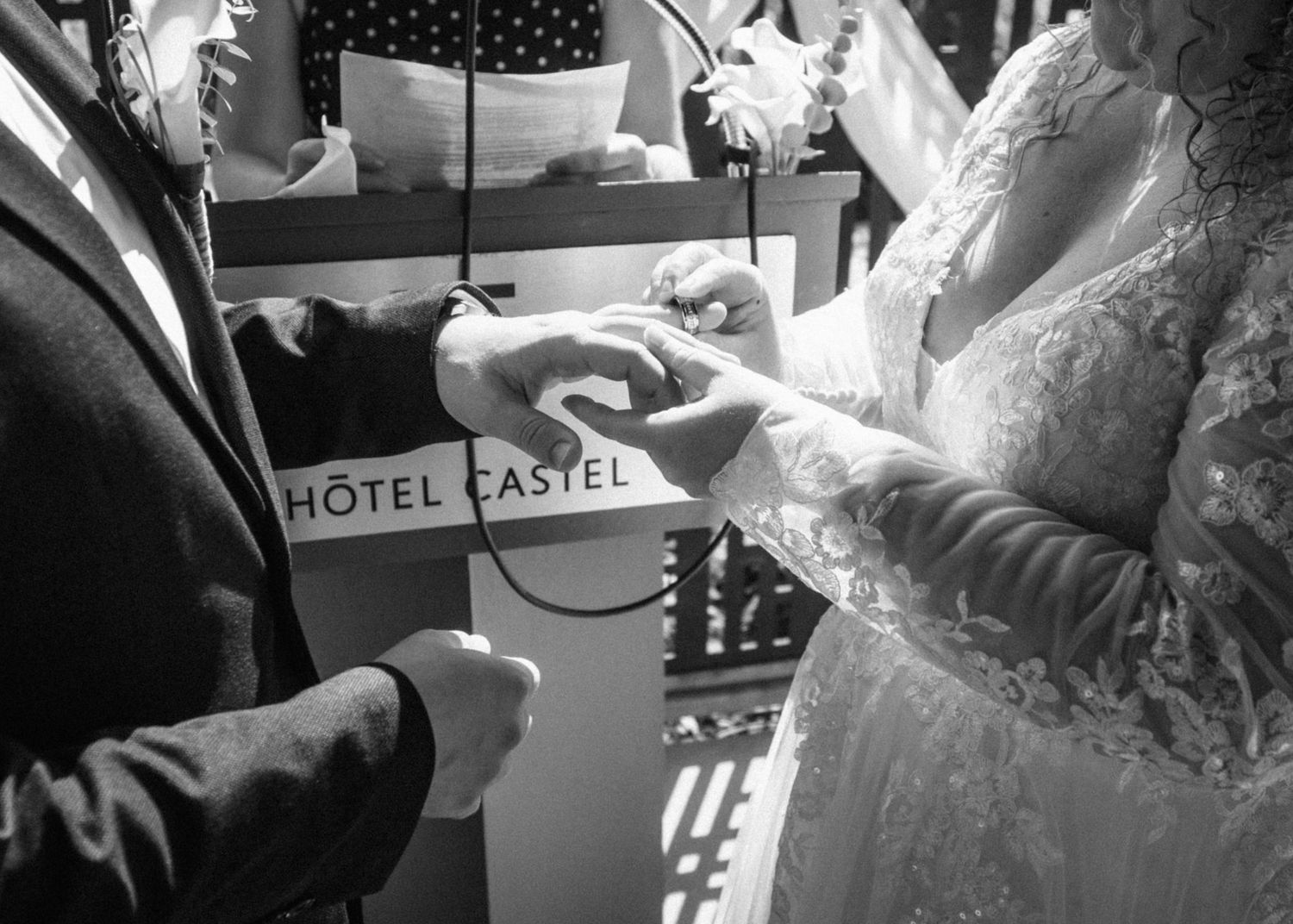 Black and white wedding ring exchange ceremony at Hotel Castel, bride and groom holding hands.