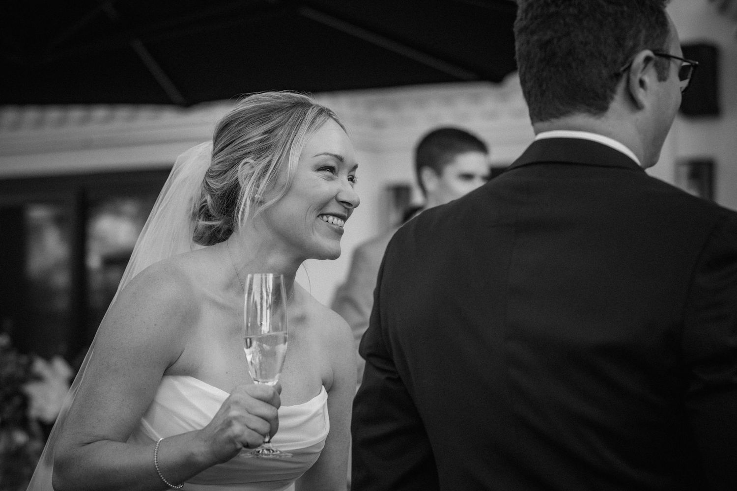 Joyful bride laughing and holding champagne glass with groom at wedding reception.