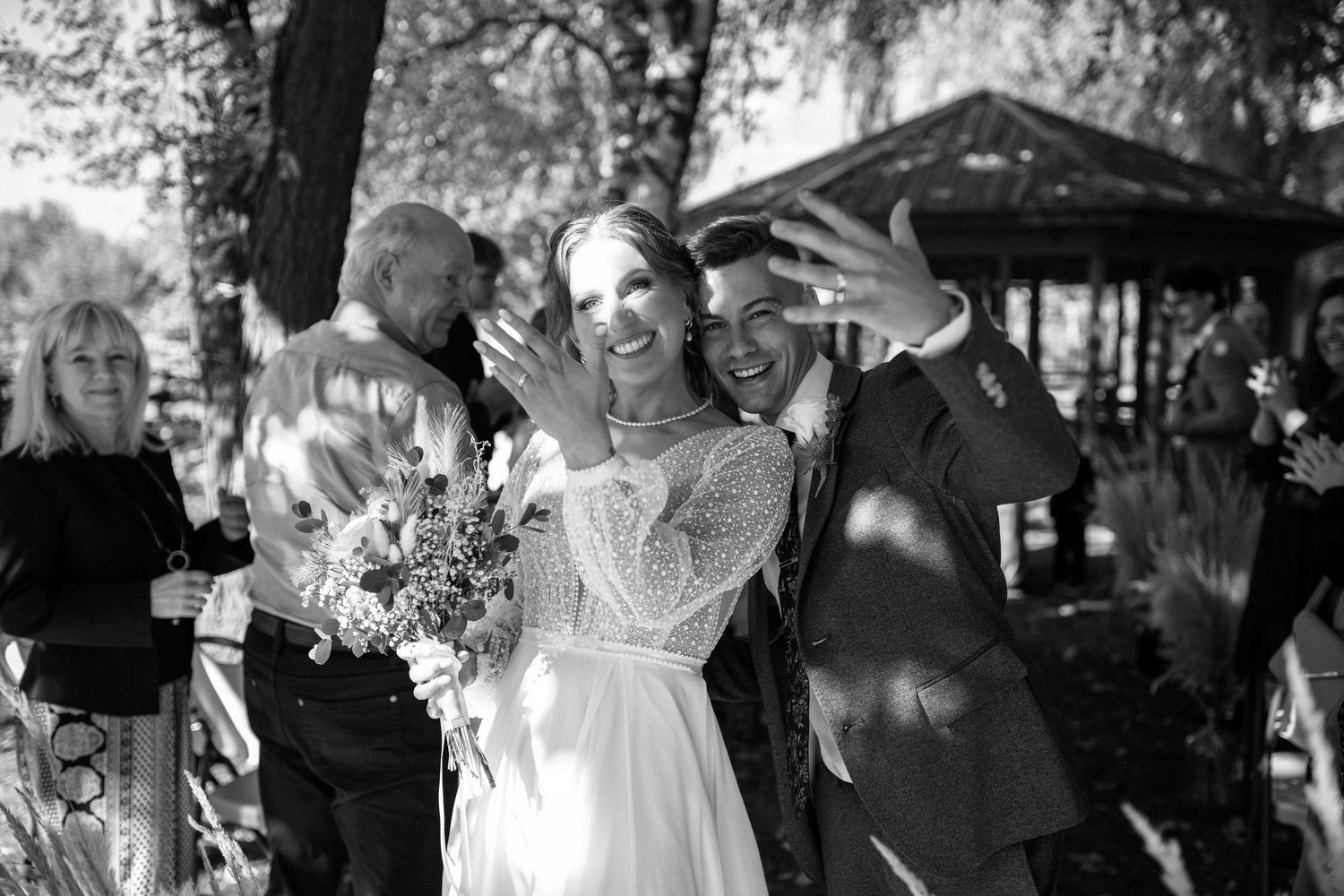 Black and white photo of smiling bride and groom showing off wedding rings after ceremony.