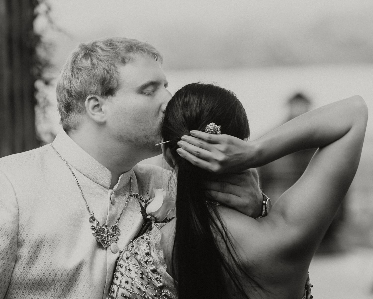 Black and white photo of a groom kissing his bride on the head at a wedding ceremony.