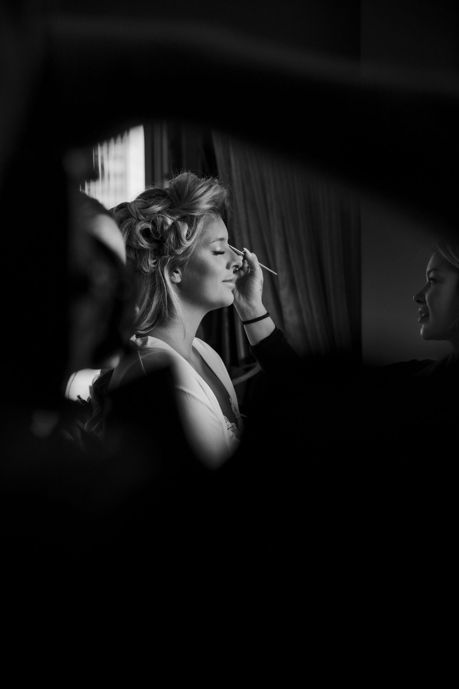 Black and white photo of a bride getting makeup applied before her wedding ceremony.