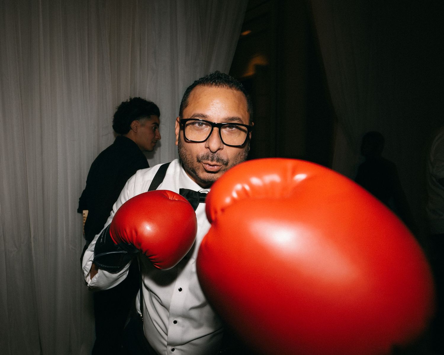 Wedding guest playfully posing with oversized red boxing gloves at a fun reception photo booth.