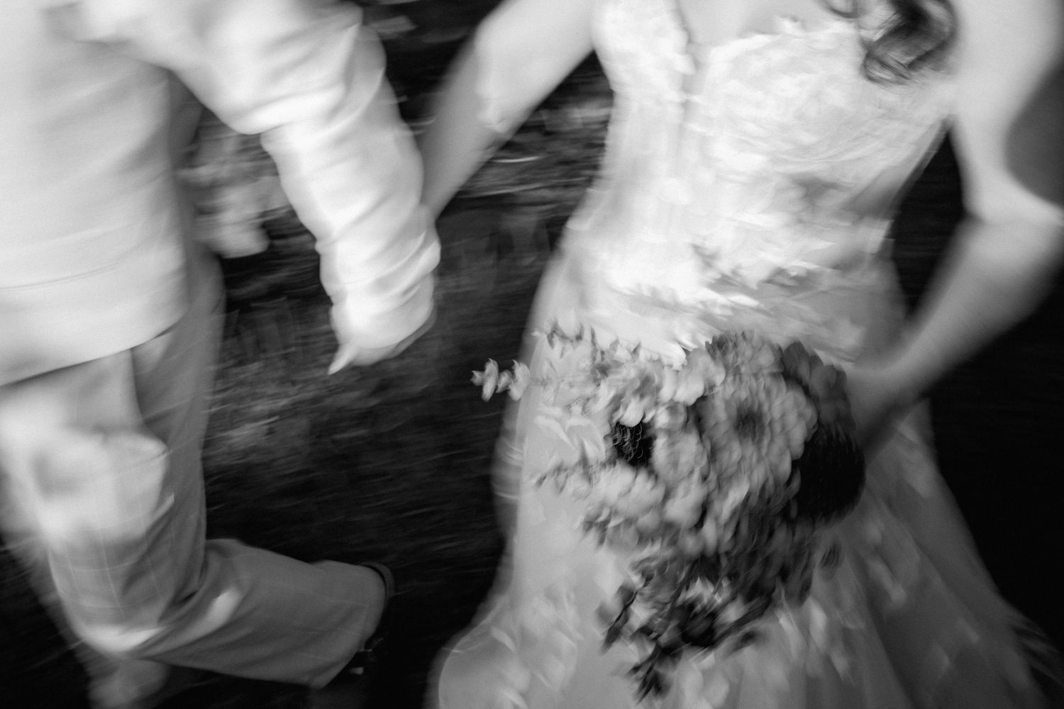 Blurred black and white photo of a bride in a wedding dress holding a bouquet, dancing with guests.