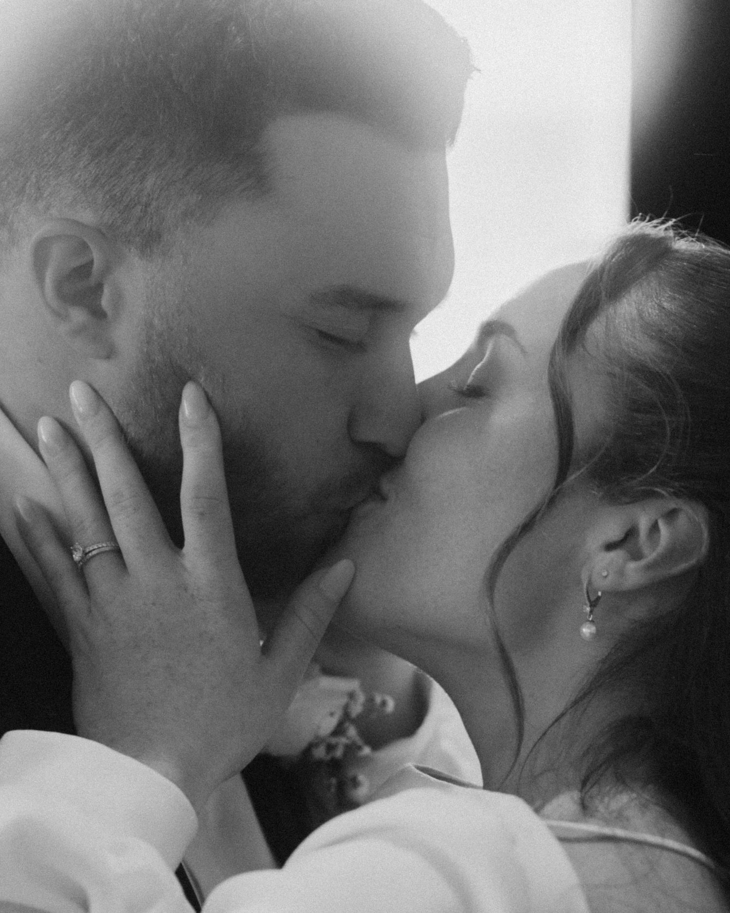 Black and white photo of a couple sharing a romantic kiss, with an engagement ring visible on her hand.