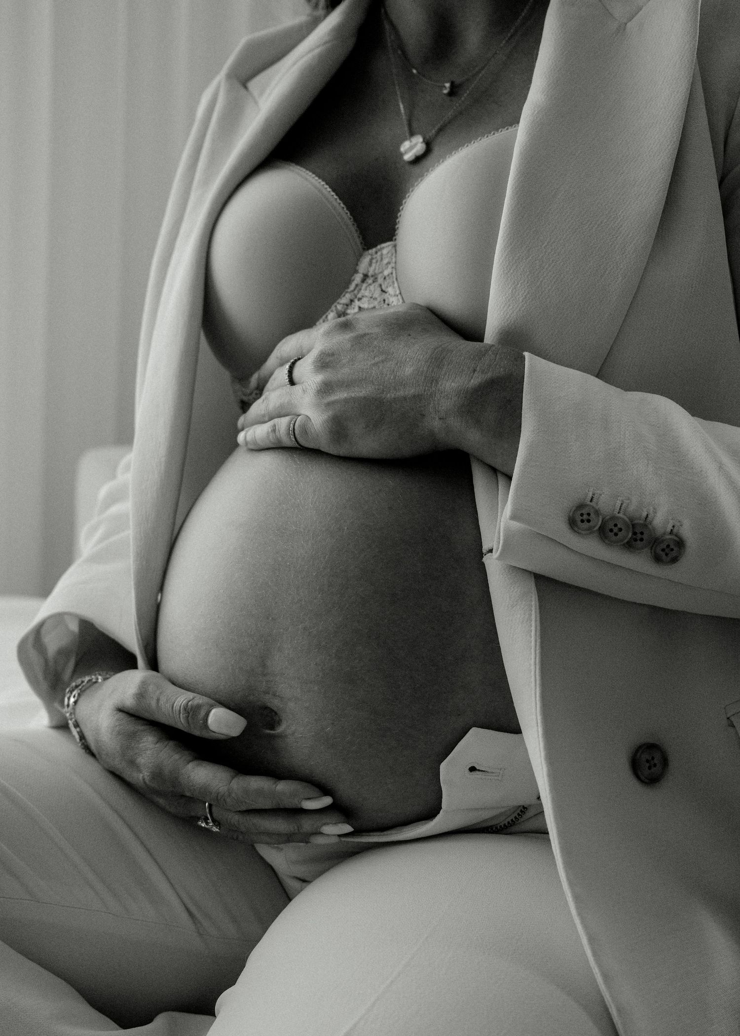 Close-up black and white photo of a pregnant woman in a white blazer with hands cradling her bare bump.