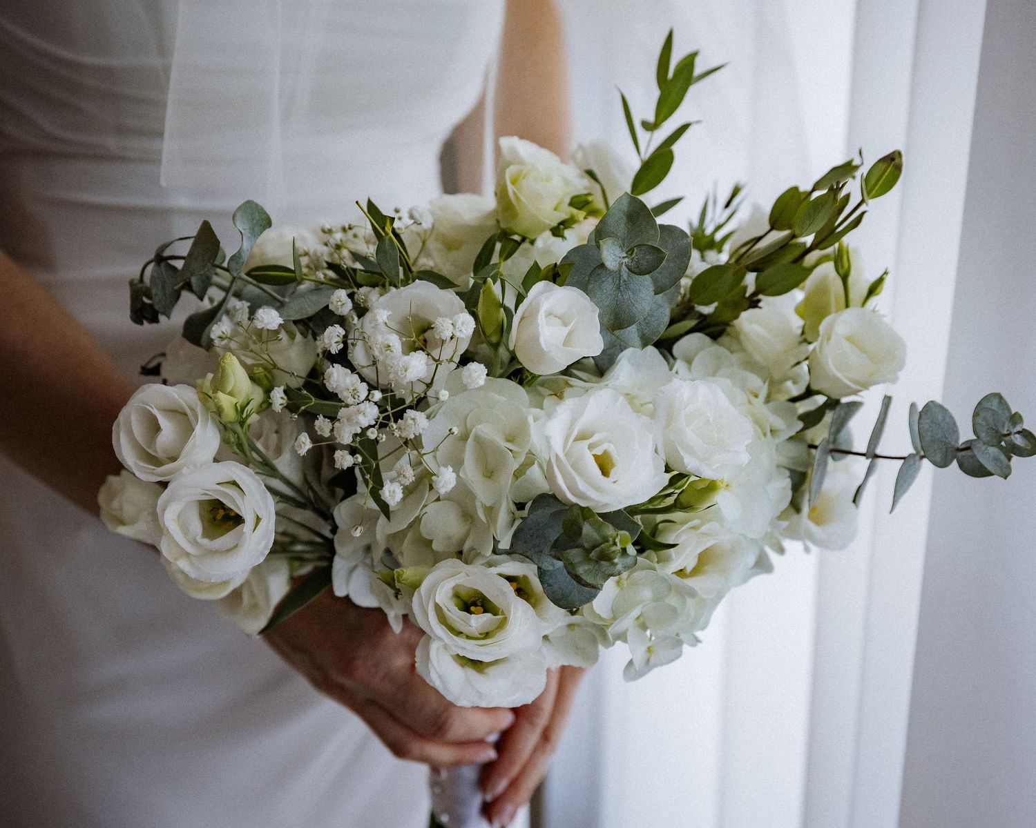 Bride holding elegant white bouquet with roses, hydrangeas, and eucalyptus greenery.