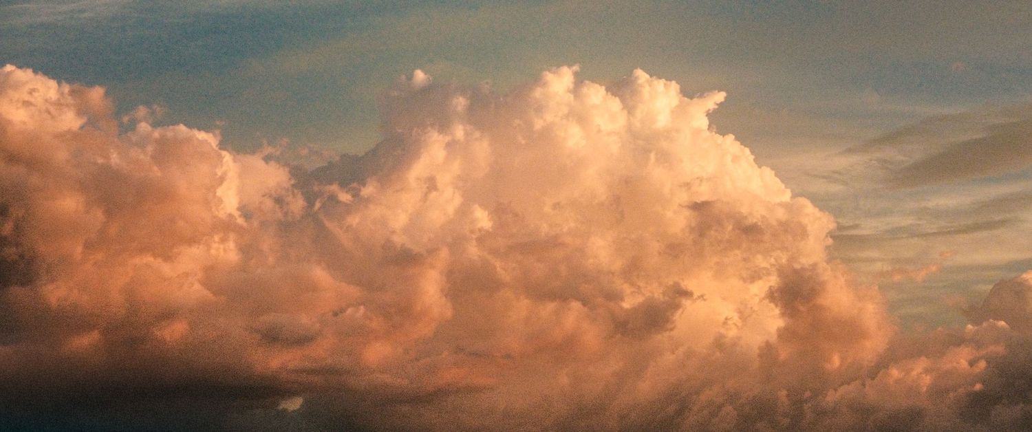Dramatic pink and orange cumulus clouds glowing at sunset against a blue sky.