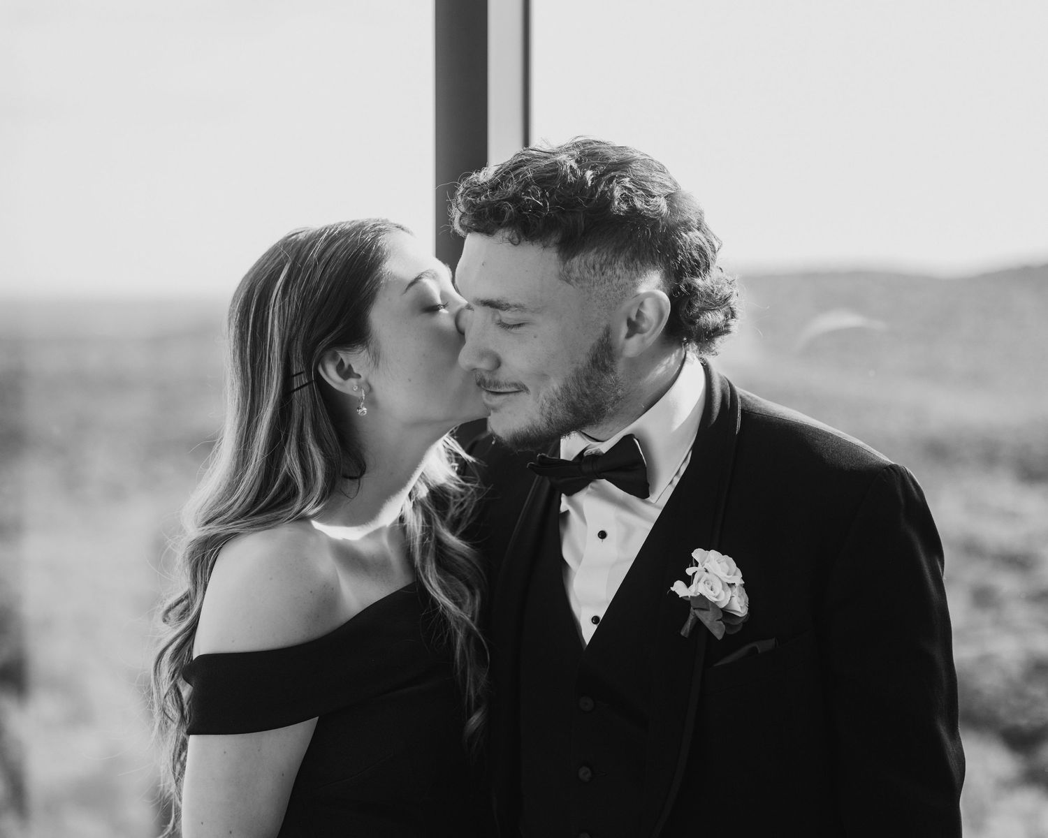 Bride and groom share a romantic kiss in elegant black and white wedding portrait.