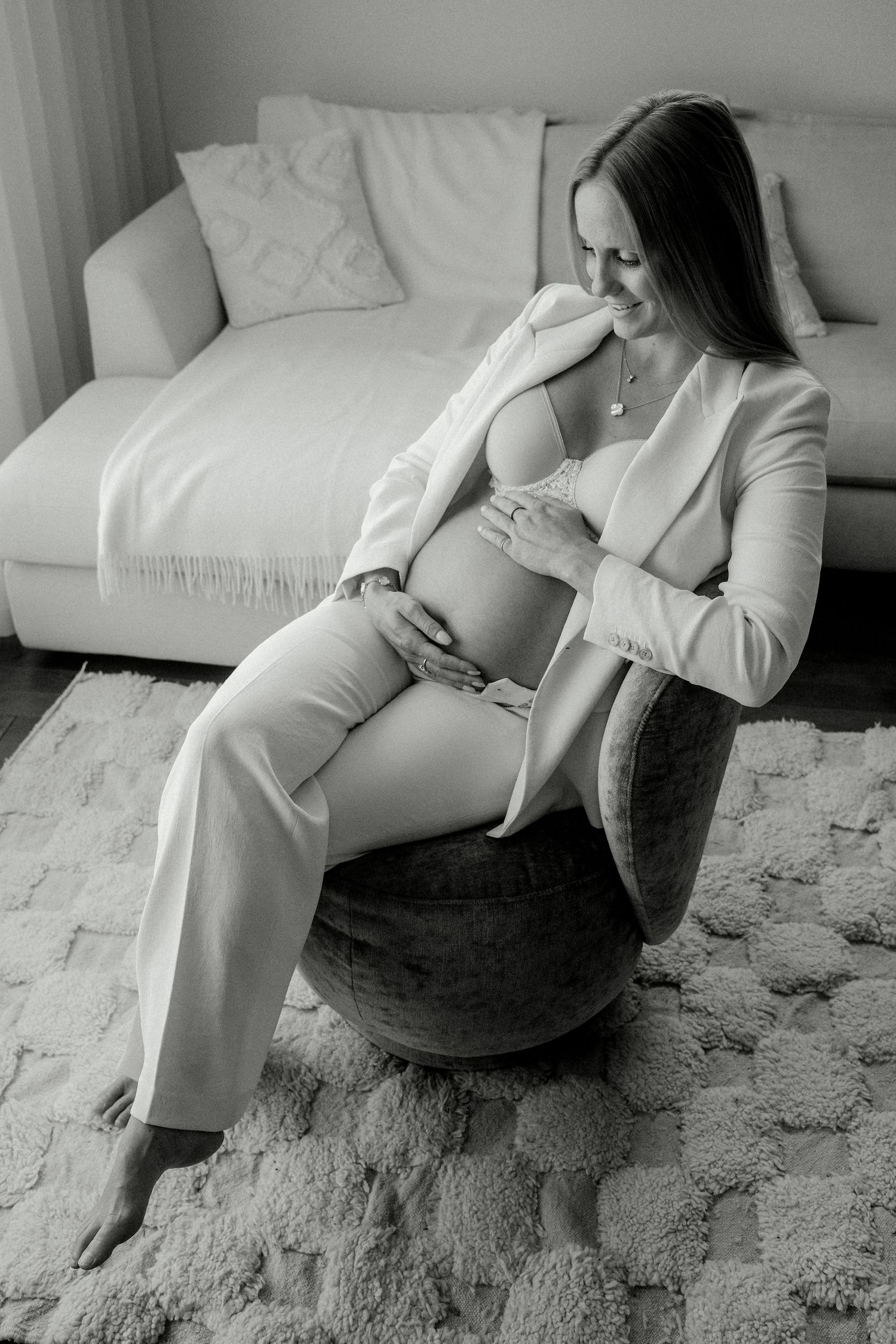 A pregnant woman in a white suit sits in a chair lovingly holding her baby bump, black and white photo.
