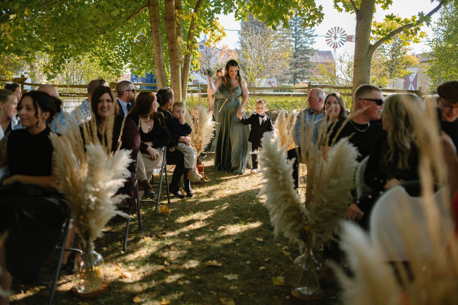 Officiant walks down the aisle lined with pampas grass at an outdoor autumn wedding ceremony.