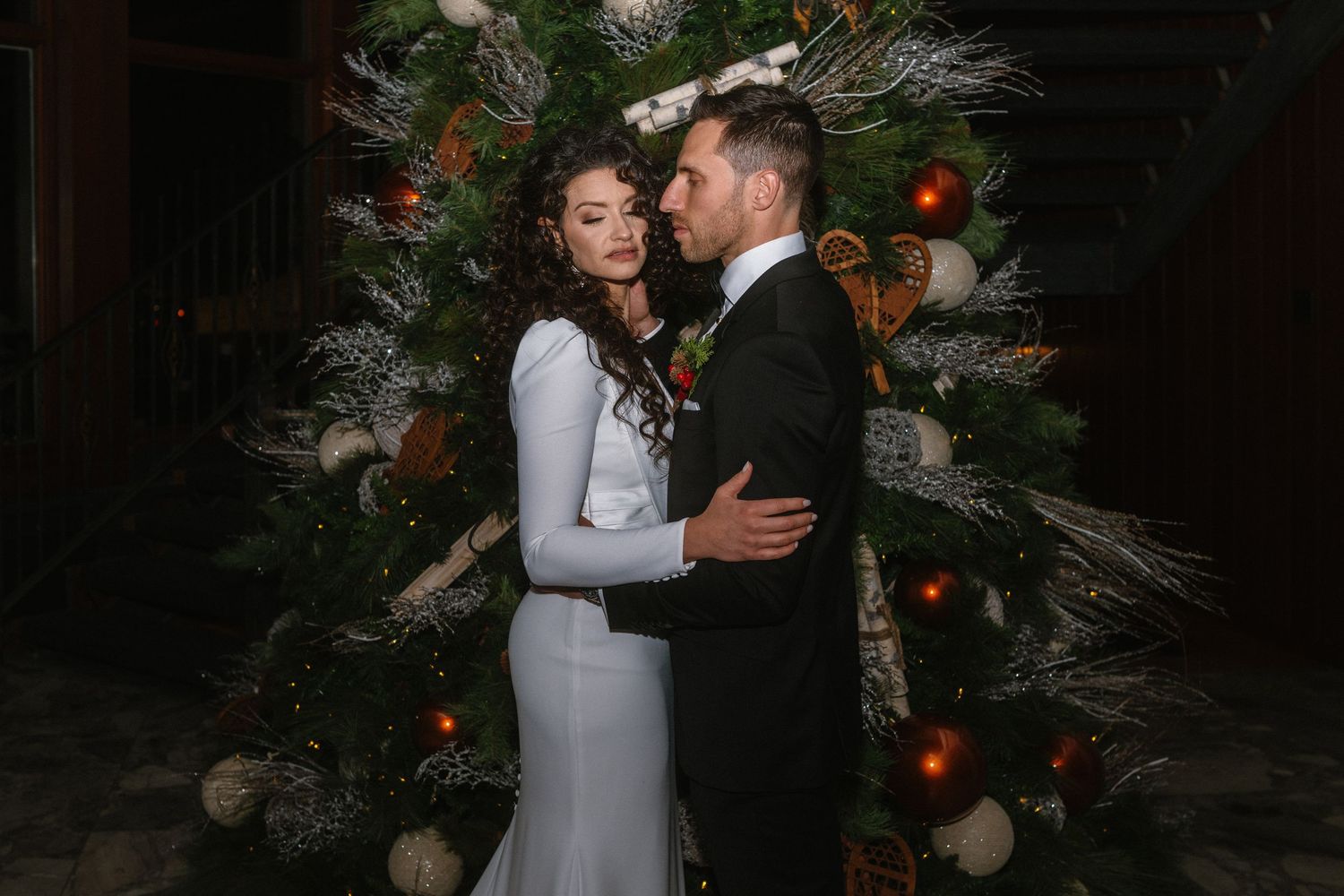 Couple embracing in front of a decorated Christmas tree at a winter wedding celebration.