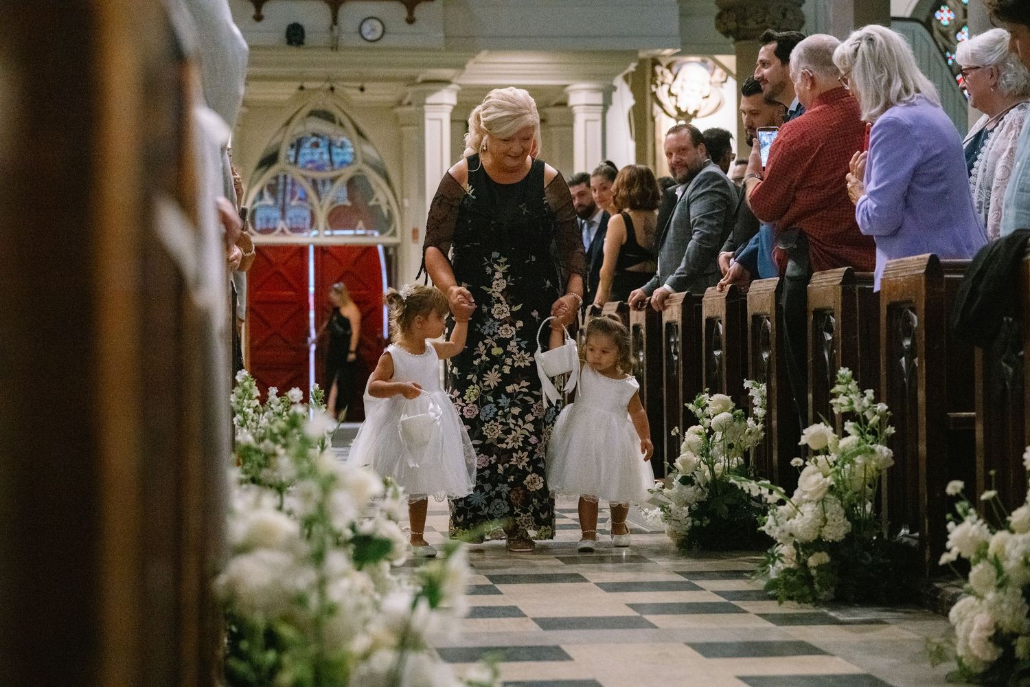 Flower girls walking down church aisle with bouquets during a wedding ceremony.
