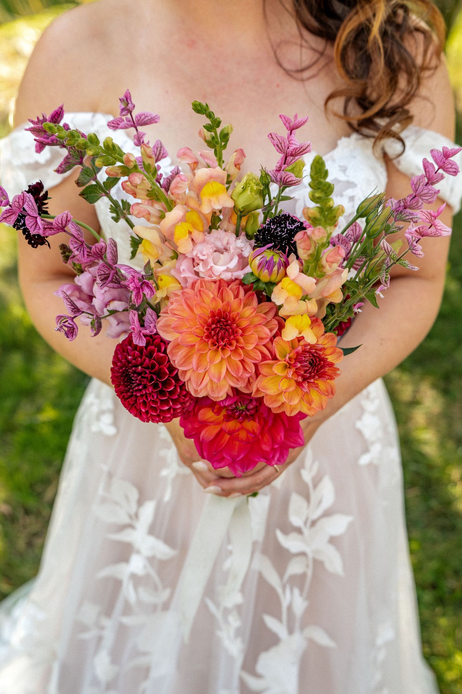 Bride holding a vibrant bouquet of dahlias and wildflowers in pink, orange, and red hues.
