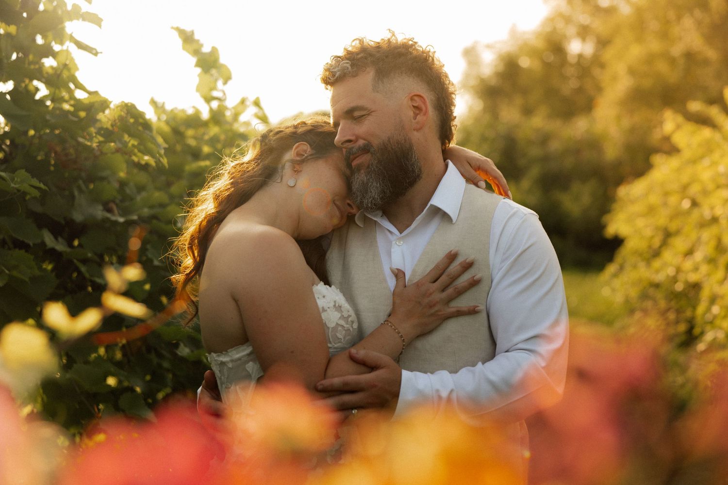 Bride and groom embracing in a flower garden at golden sunset.