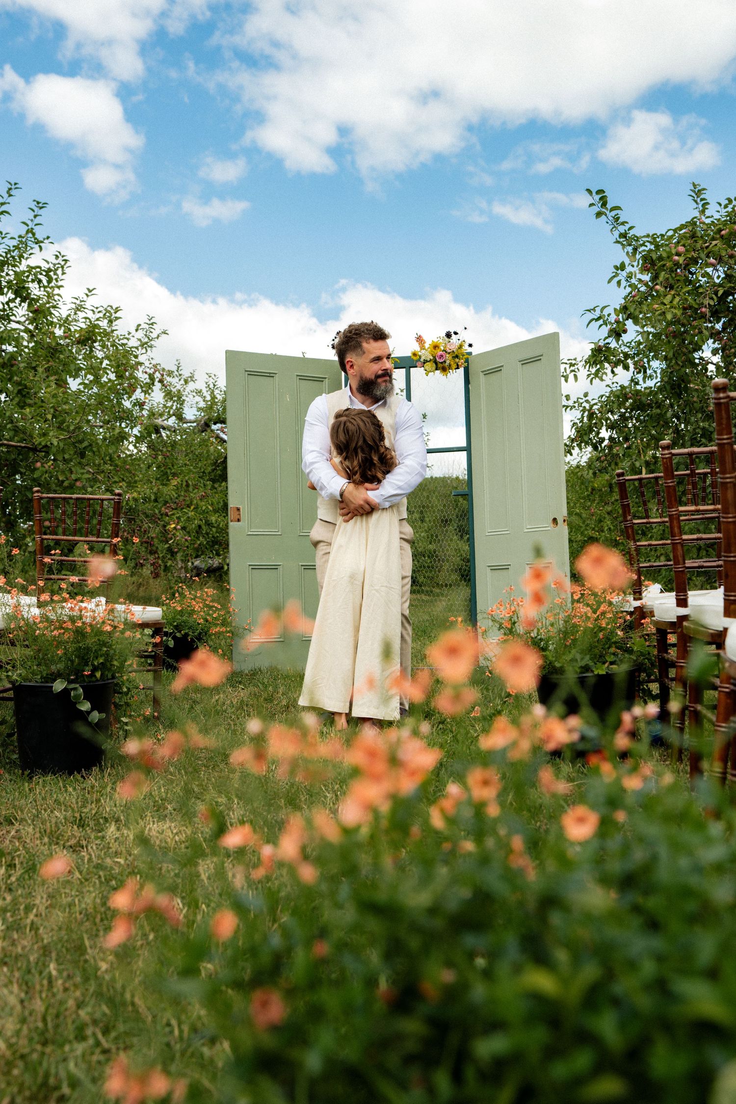 Bride and groom embrace near vintage green doors at a colorful outdoor garden wedding ceremony.