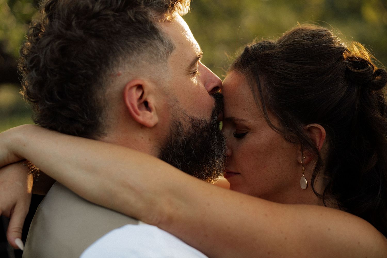 Bride and bearded groom share an intimate close moment together in warm golden sunset light.