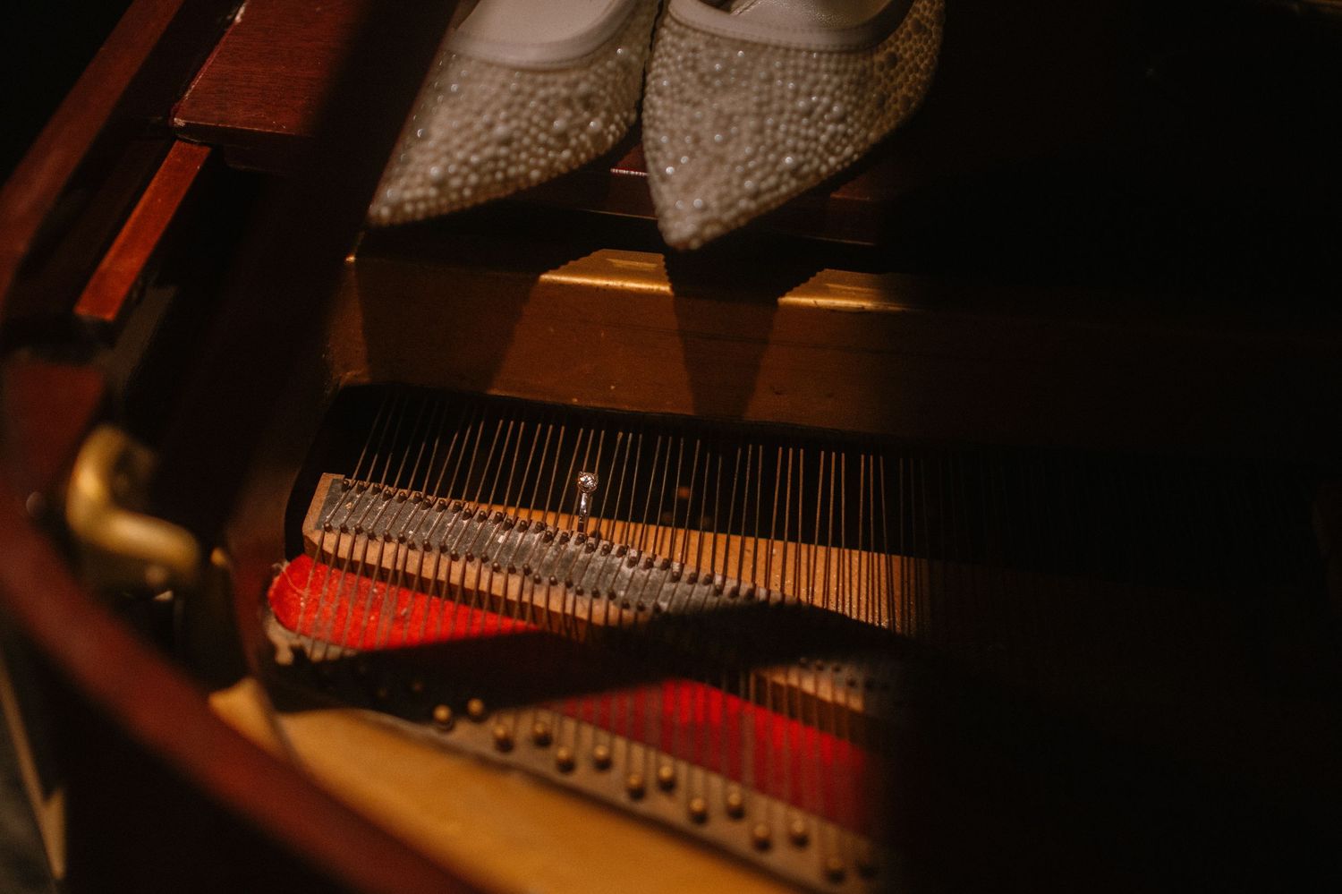 Sparkling bridal heels resting on the strings inside an open grand piano in warm light.
