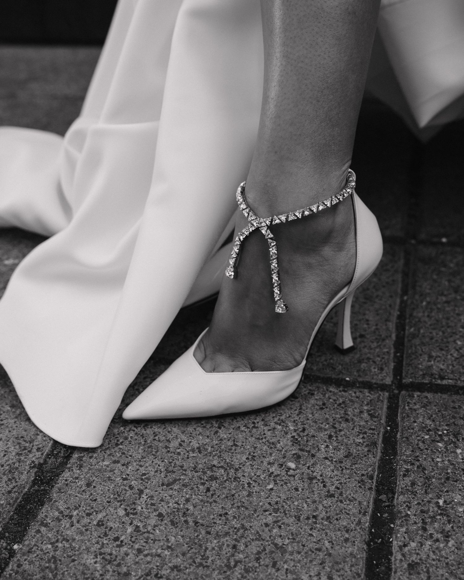 Bride wearing elegant white pointed-toe heels adorned with a sparkling crystal anklet bracelet.