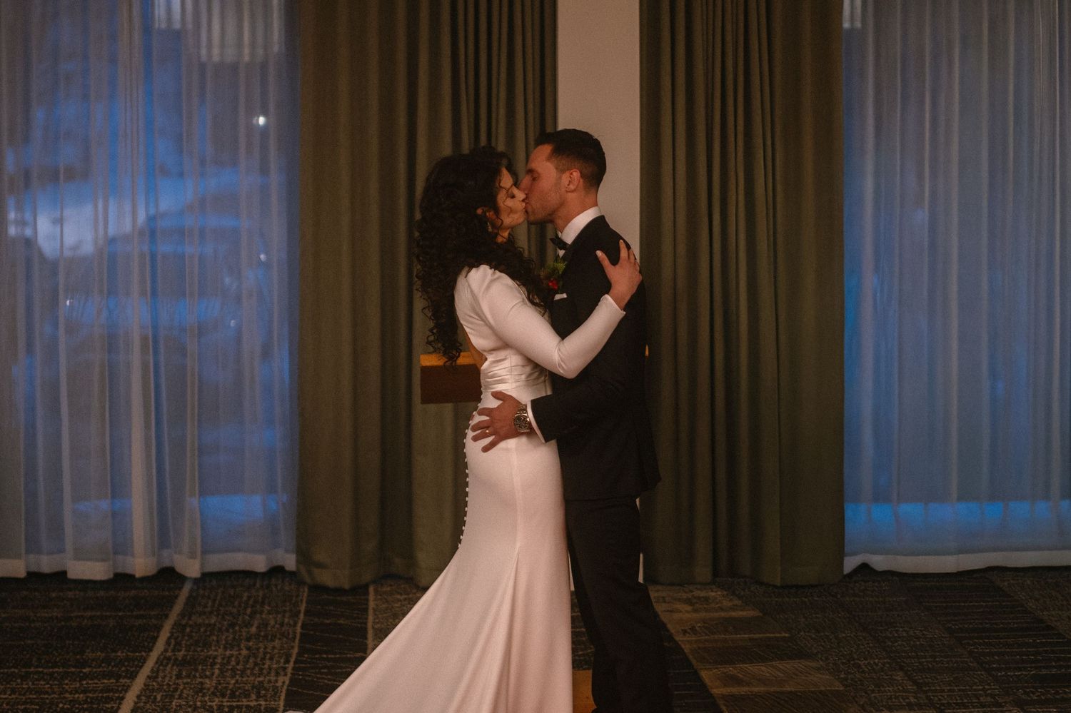 A bride and groom share a romantic first dance kiss in a dimly lit ballroom, bride wearing elegant white gown.