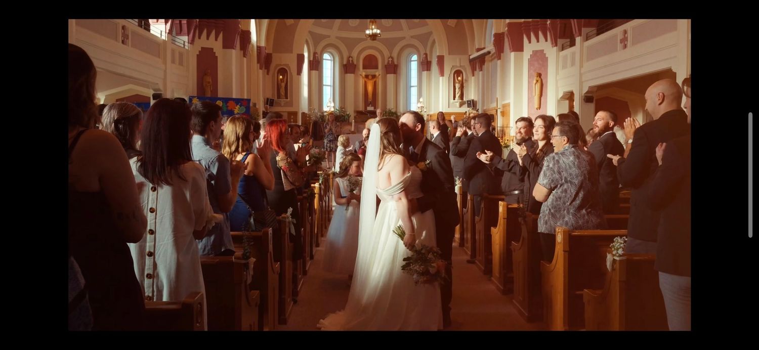 Bride in white gown and veil walks down church aisle surrounded by guests during traditional wedding ceremony.
