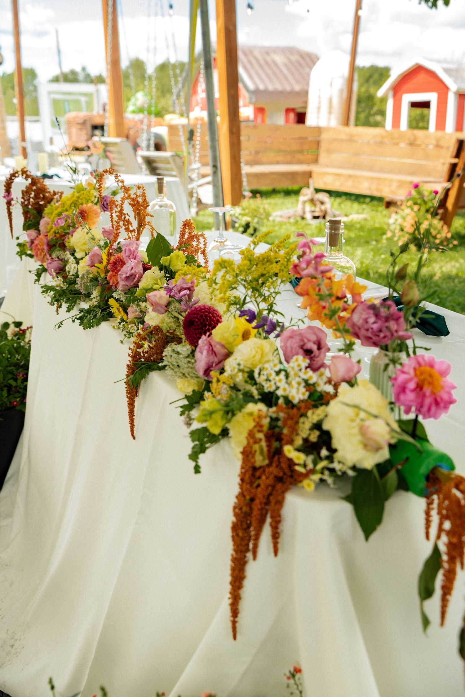 Colorful floral centerpiece with peonies and hanging amaranth on a white tablecloth at a wedding reception.