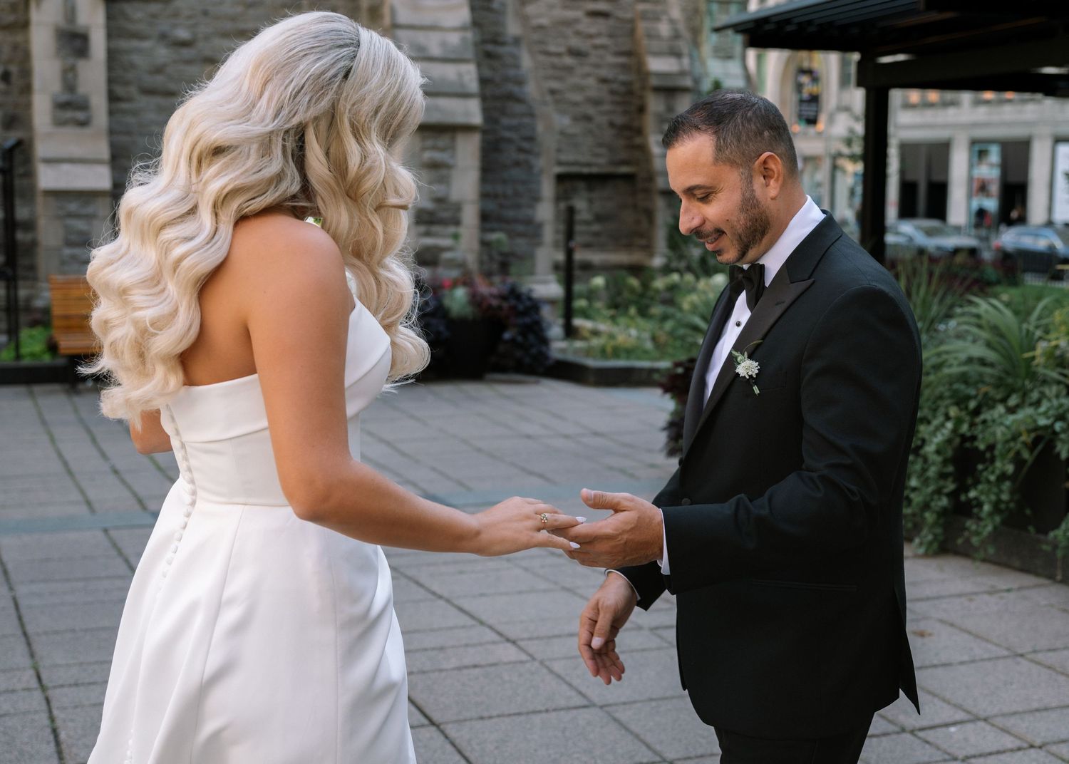 Bride and groom exchanging rings outdoors at an urban wedding venue.