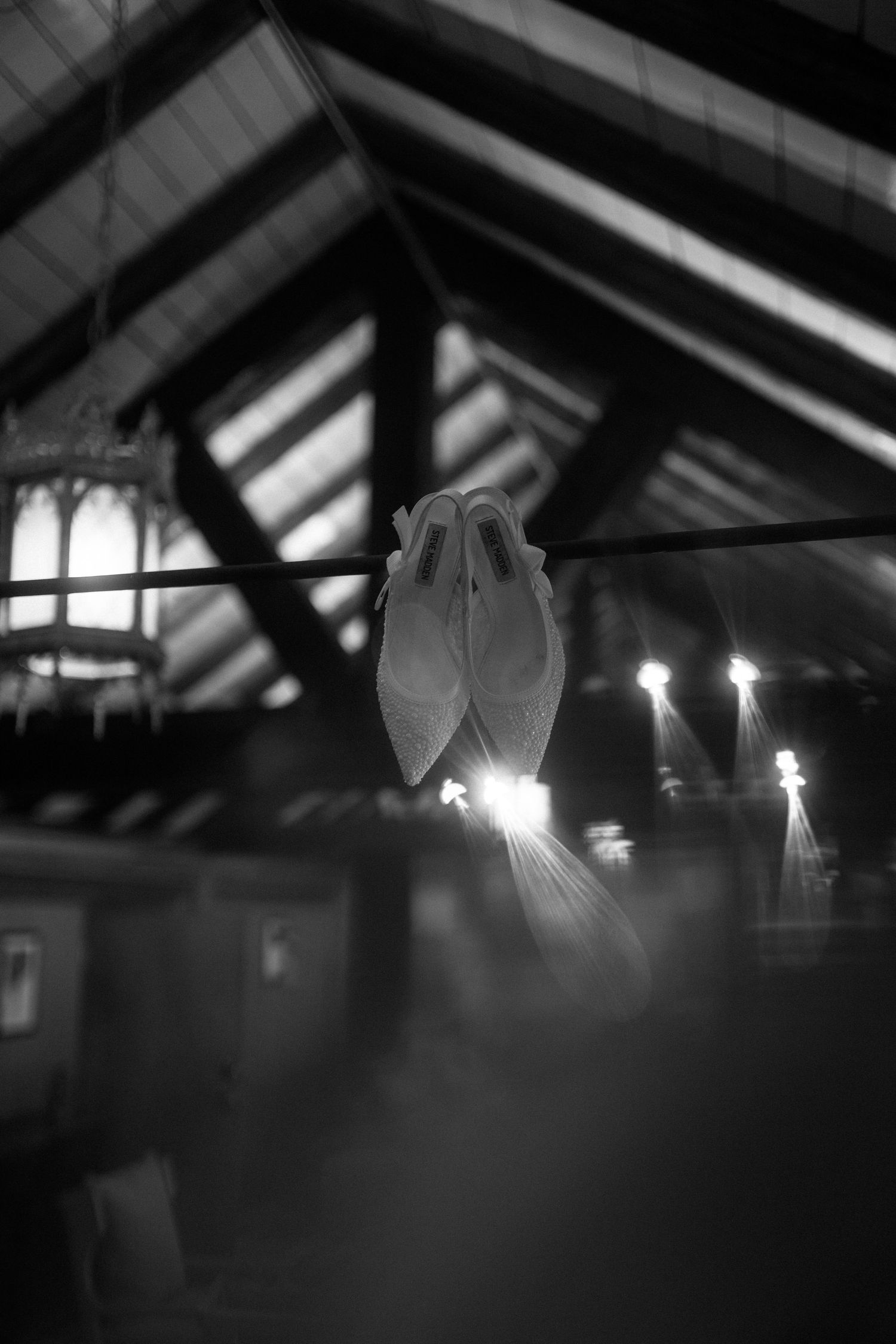 Black and white photo of a delicate paper bird ornament hanging in a rustic venue with glowing lights.