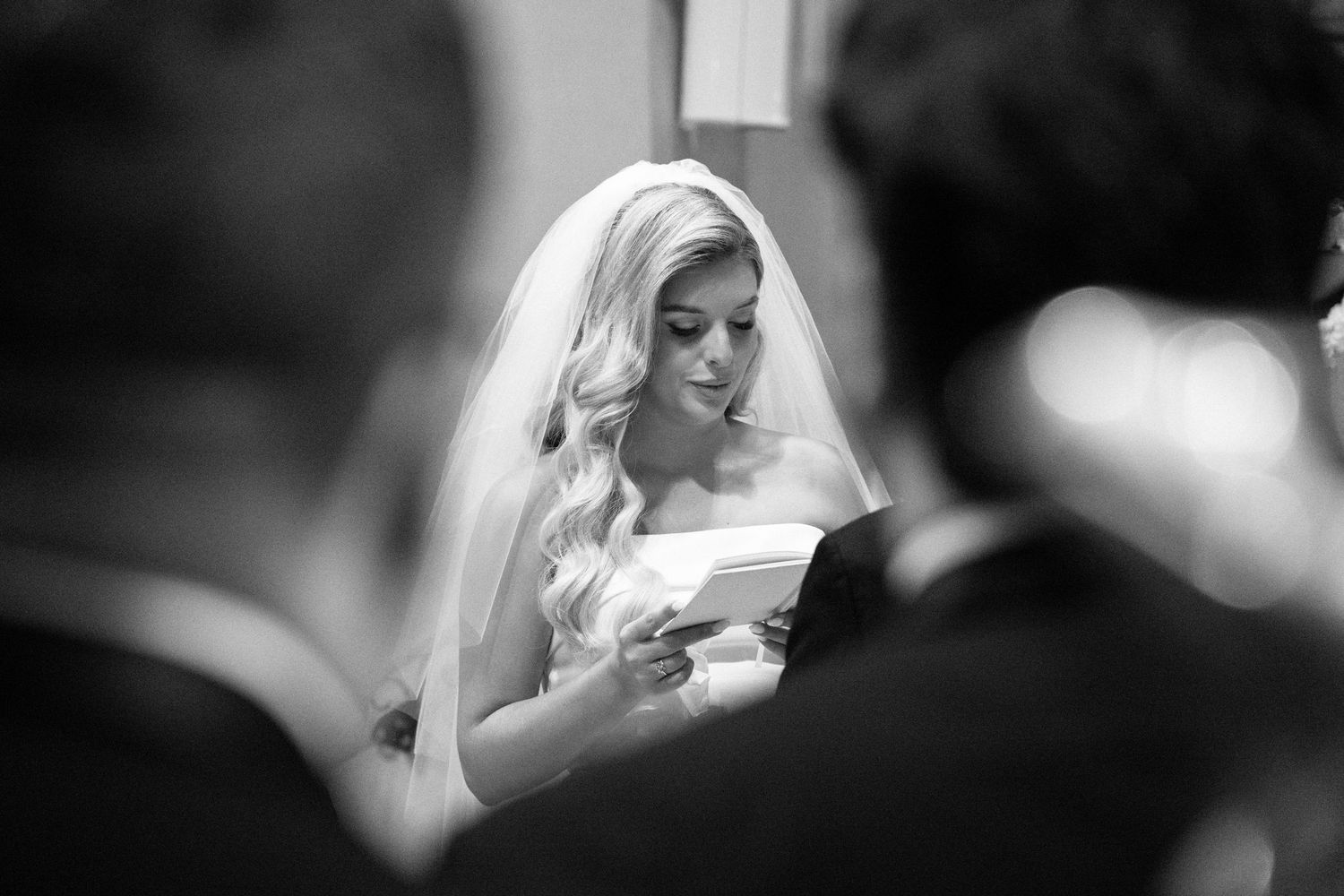 Blonde bride in veil reading wedding vows during church ceremony in black and white.