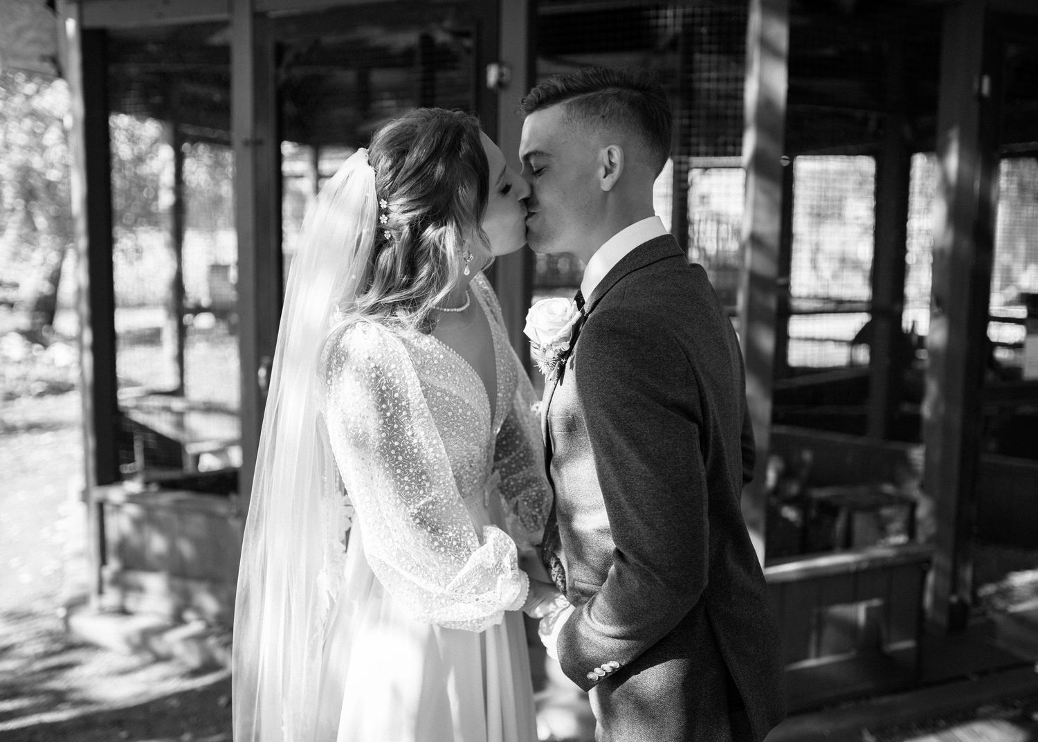 Bride and groom sharing first kiss at outdoor wedding ceremony in black and white photo.