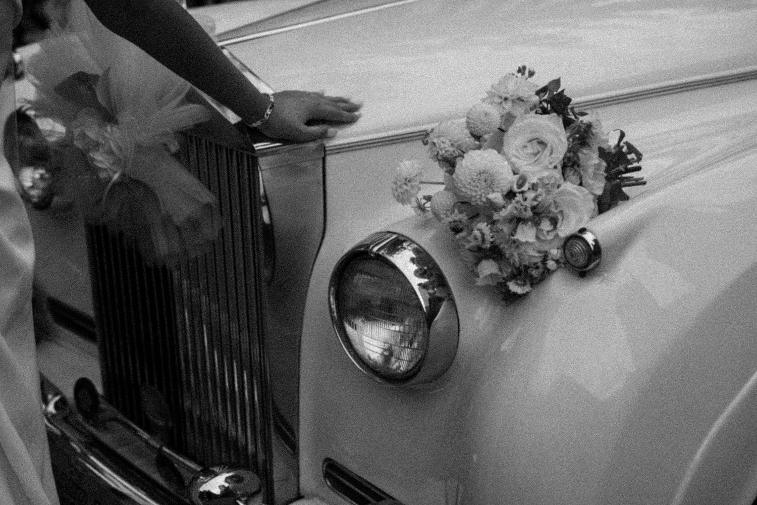 Bridal bouquet of white flowers resting on the hood of a classic vintage white Rolls-Royce.