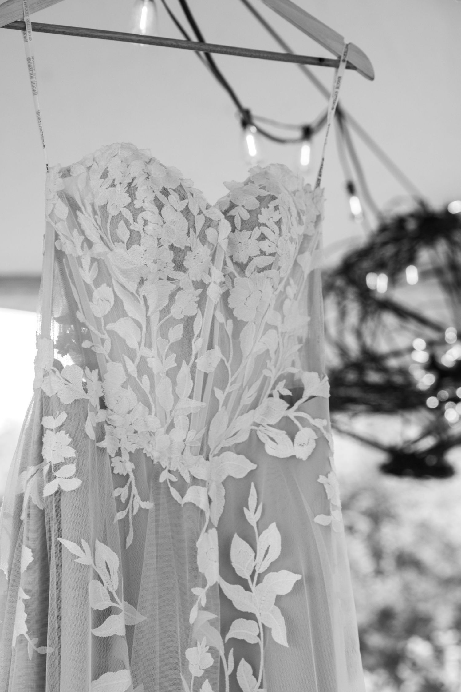 Elegant strapless wedding dress with floral lace applique hanging on a hanger in black and white.