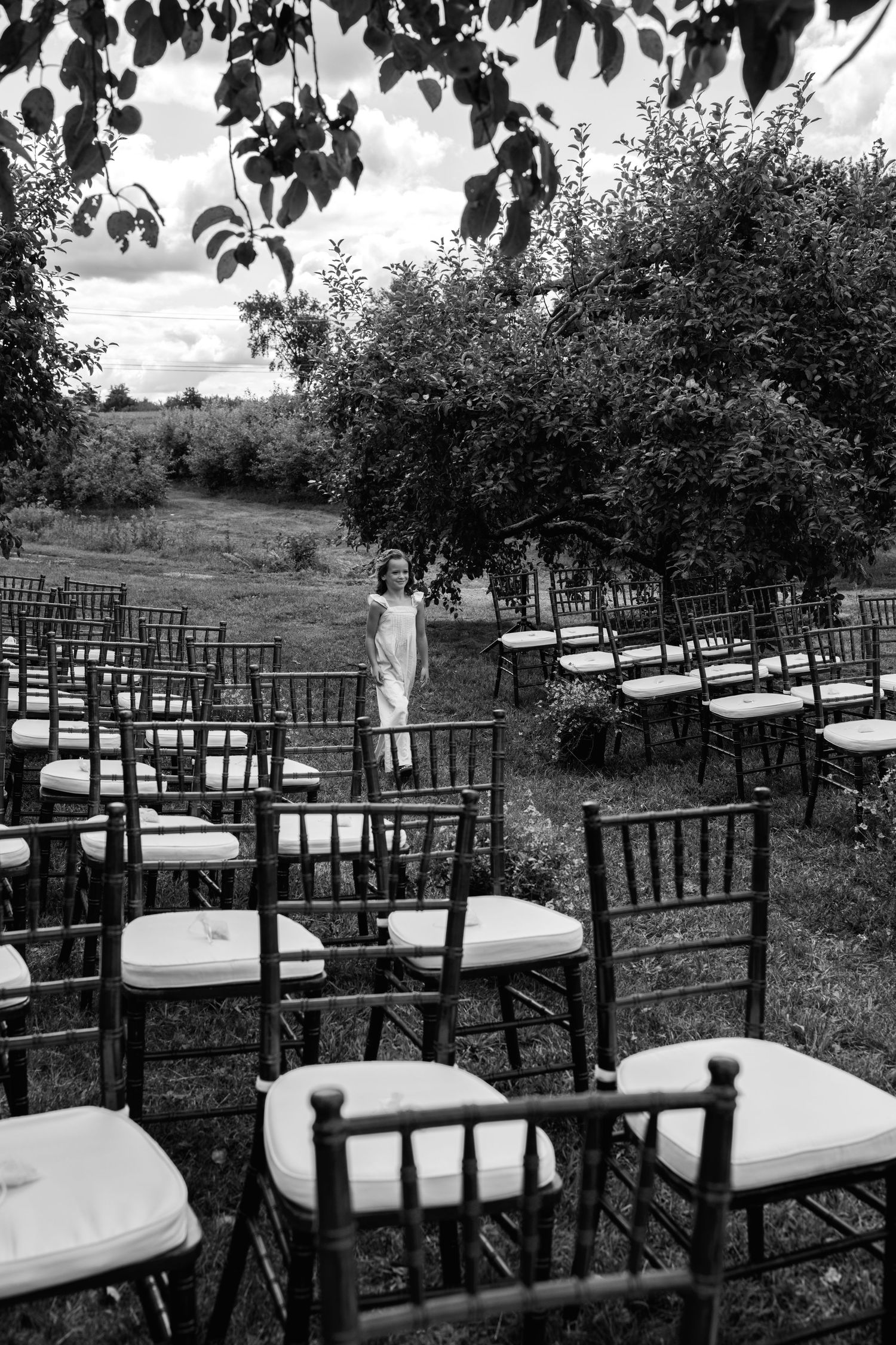 Black and white photo of empty Chiavari chairs set up for an outdoor wedding ceremony in a lush garden.