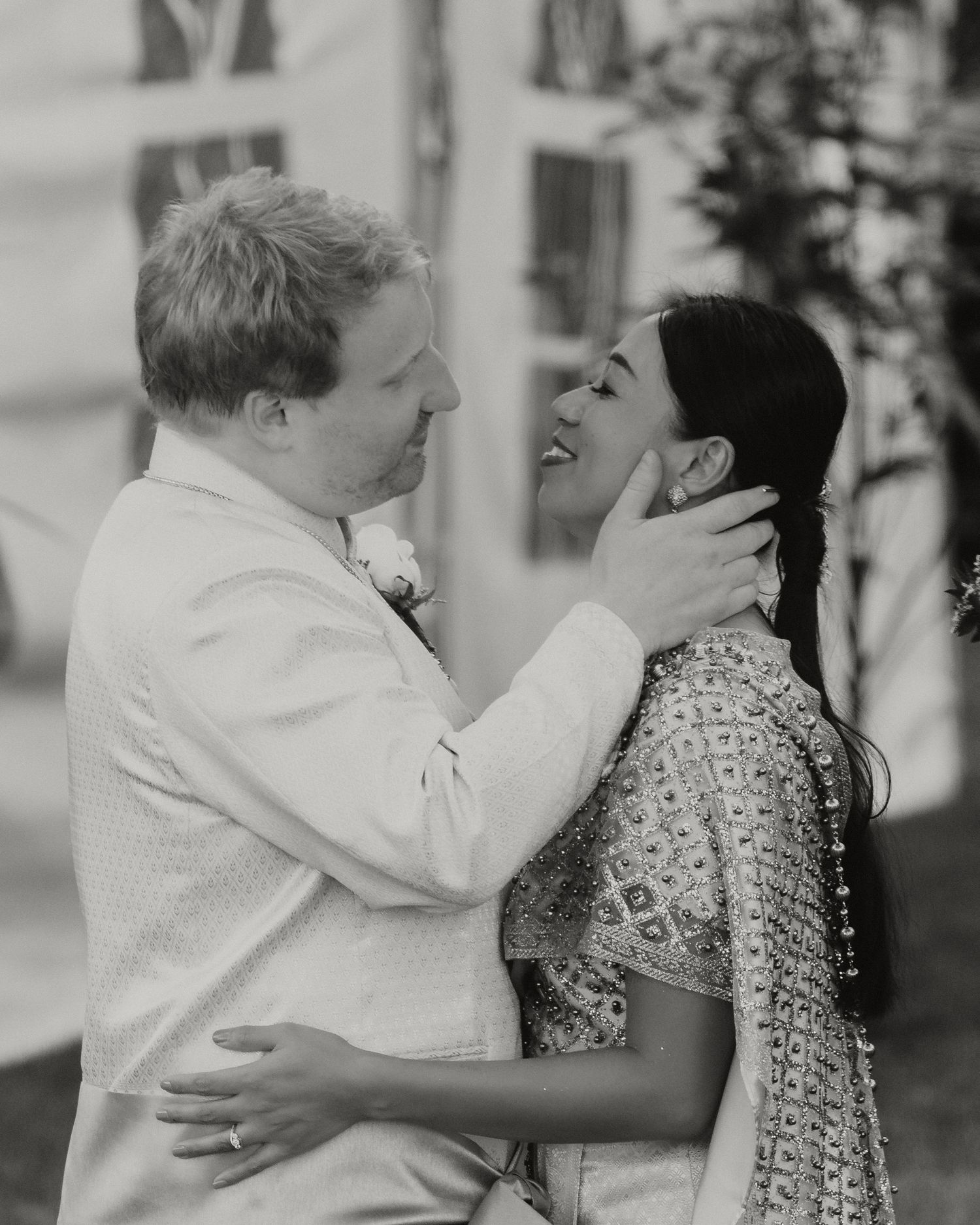 Black and white photo of a groom tenderly holding his bride's face during their outdoor wedding ceremony.