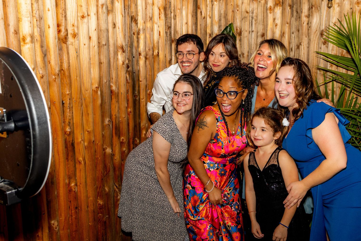 Group of friends posing together in a photo booth with wooden backdrop at a festive event.