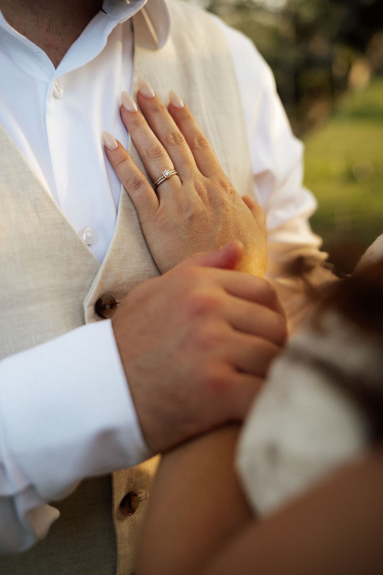 Close-up of bride's hand with wedding ring resting on groom's cream vest at their wedding.