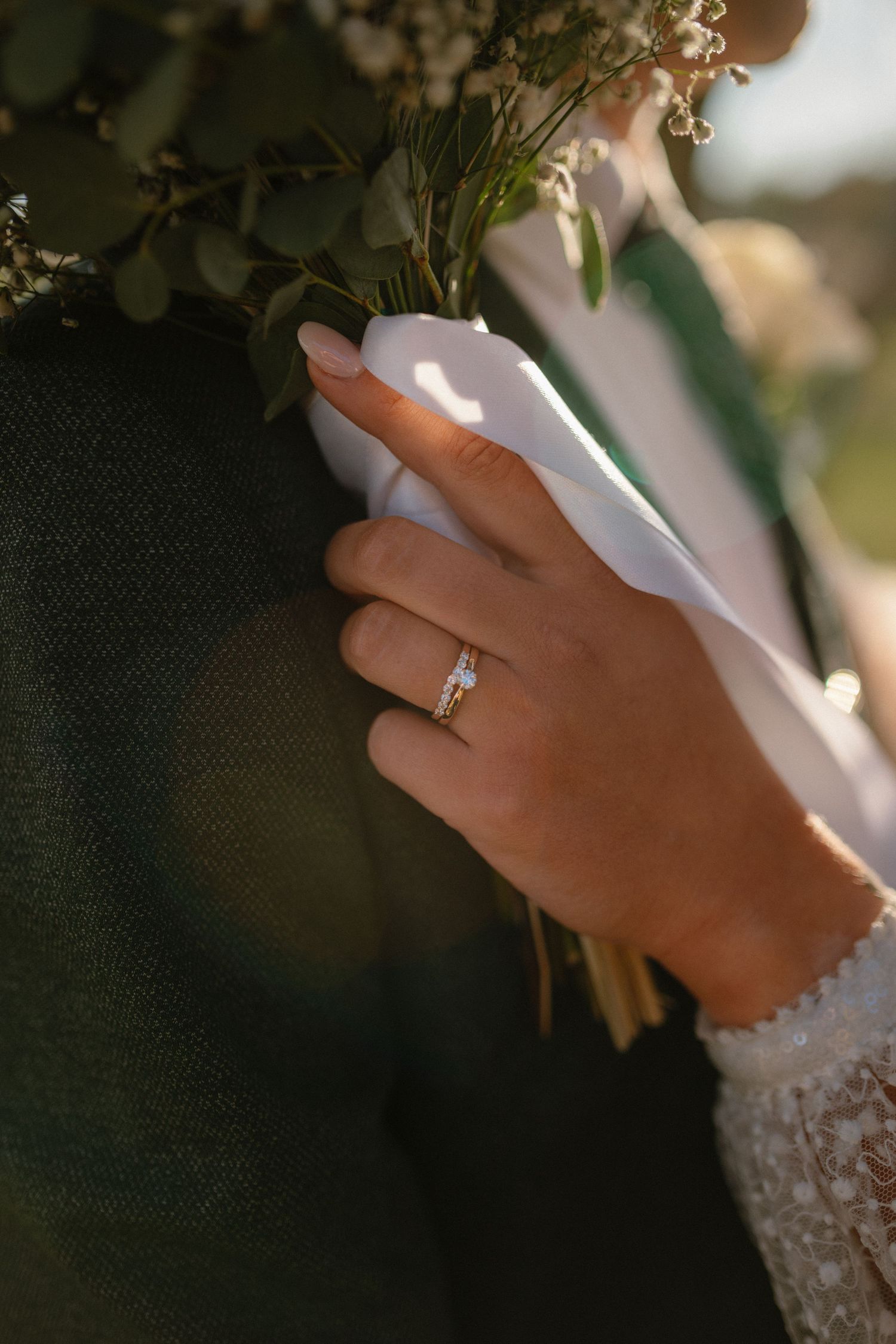 Close-up of bride's hand holding floral bouquet with elegant diamond engagement ring.