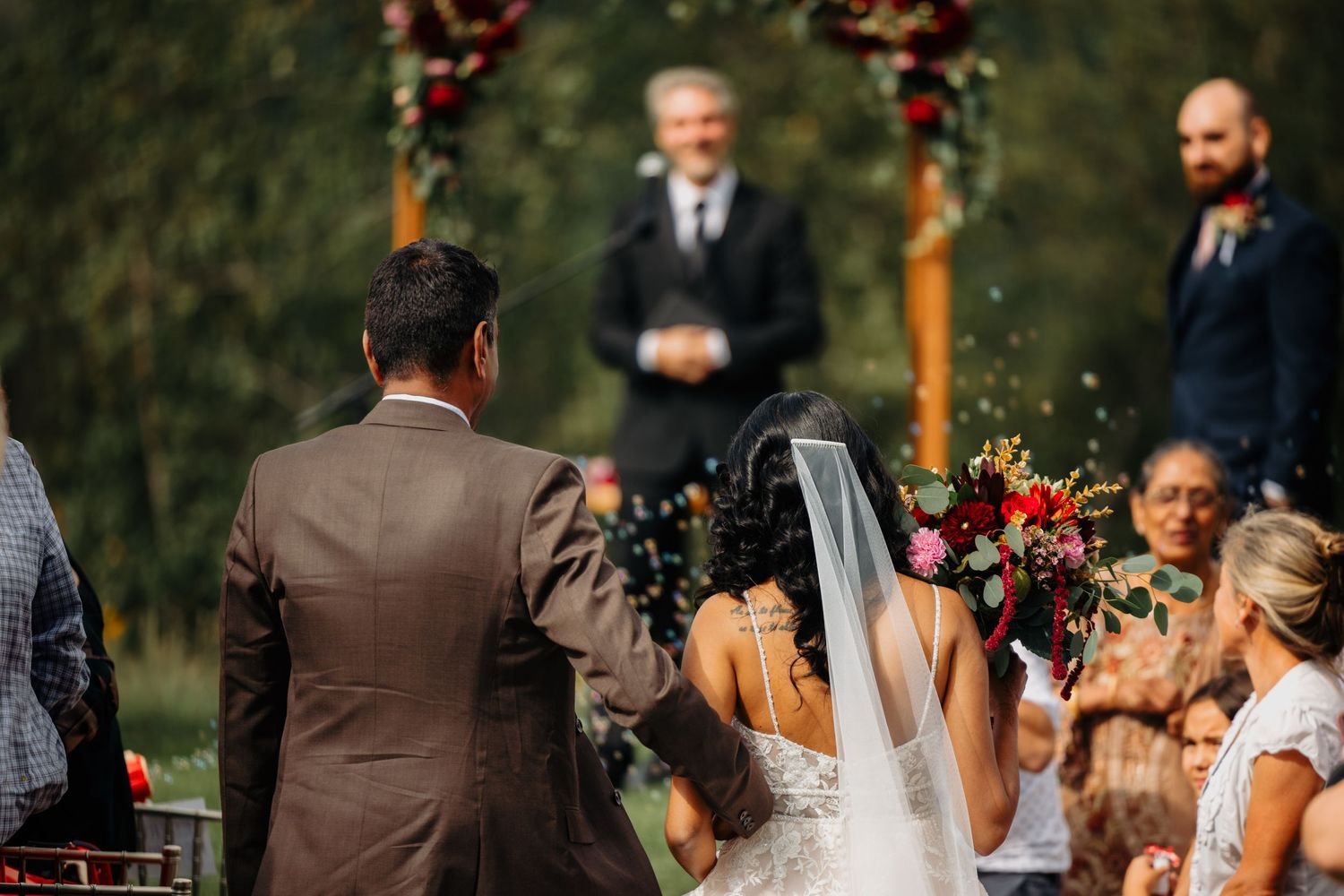 Bride and groom walk down the aisle at an outdoor wedding ceremony with floral arch and officiant.
