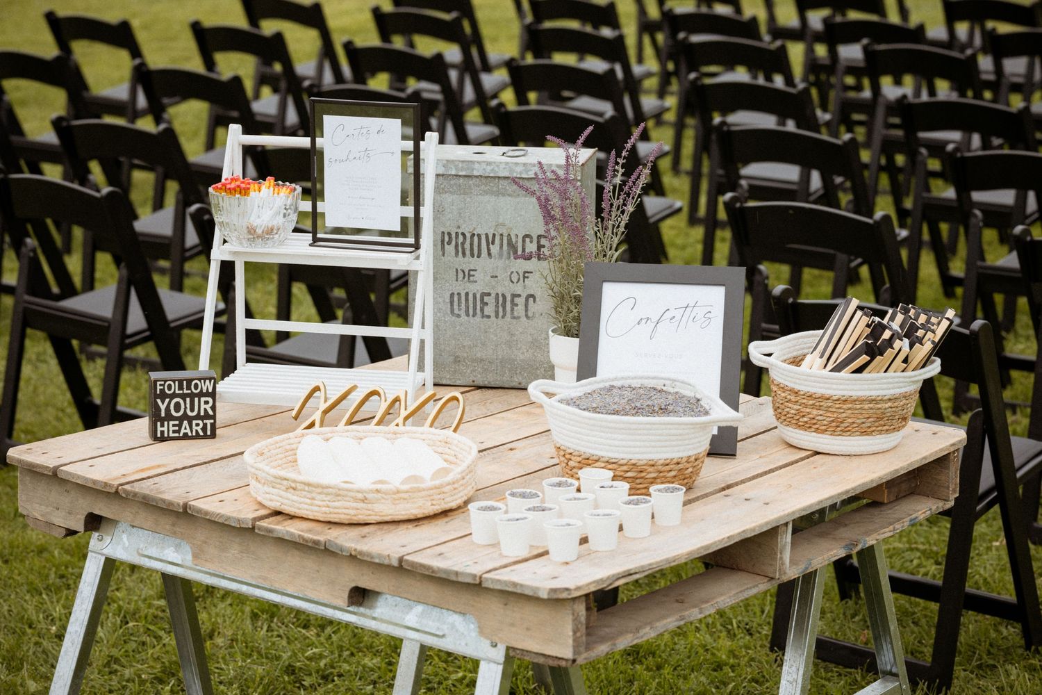 Rustic wedding welcome table with Province of Quebec sign, confetti, and woven baskets on pallet wood sawhorse table.