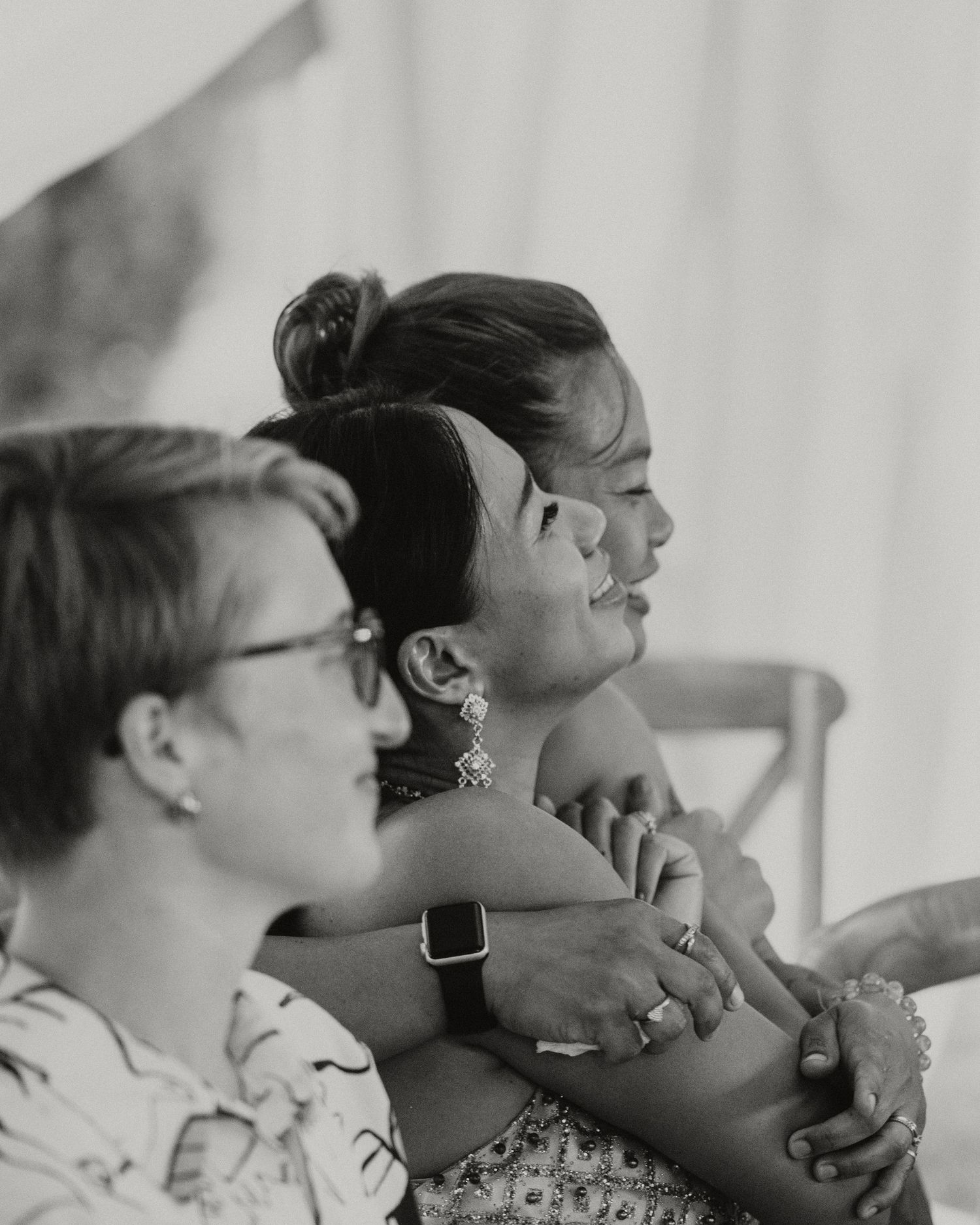 Black and white photo of two women smiling and embracing at a wedding celebration outdoors.
