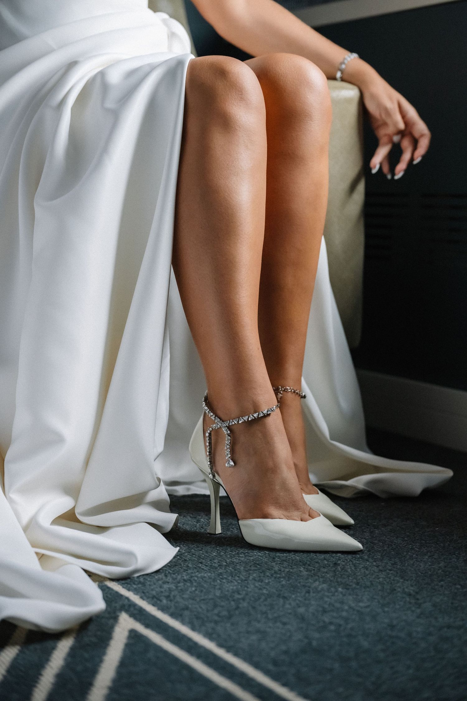 Bride wearing elegant white satin heels with crystal ankle straps, paired with a flowing white wedding gown.