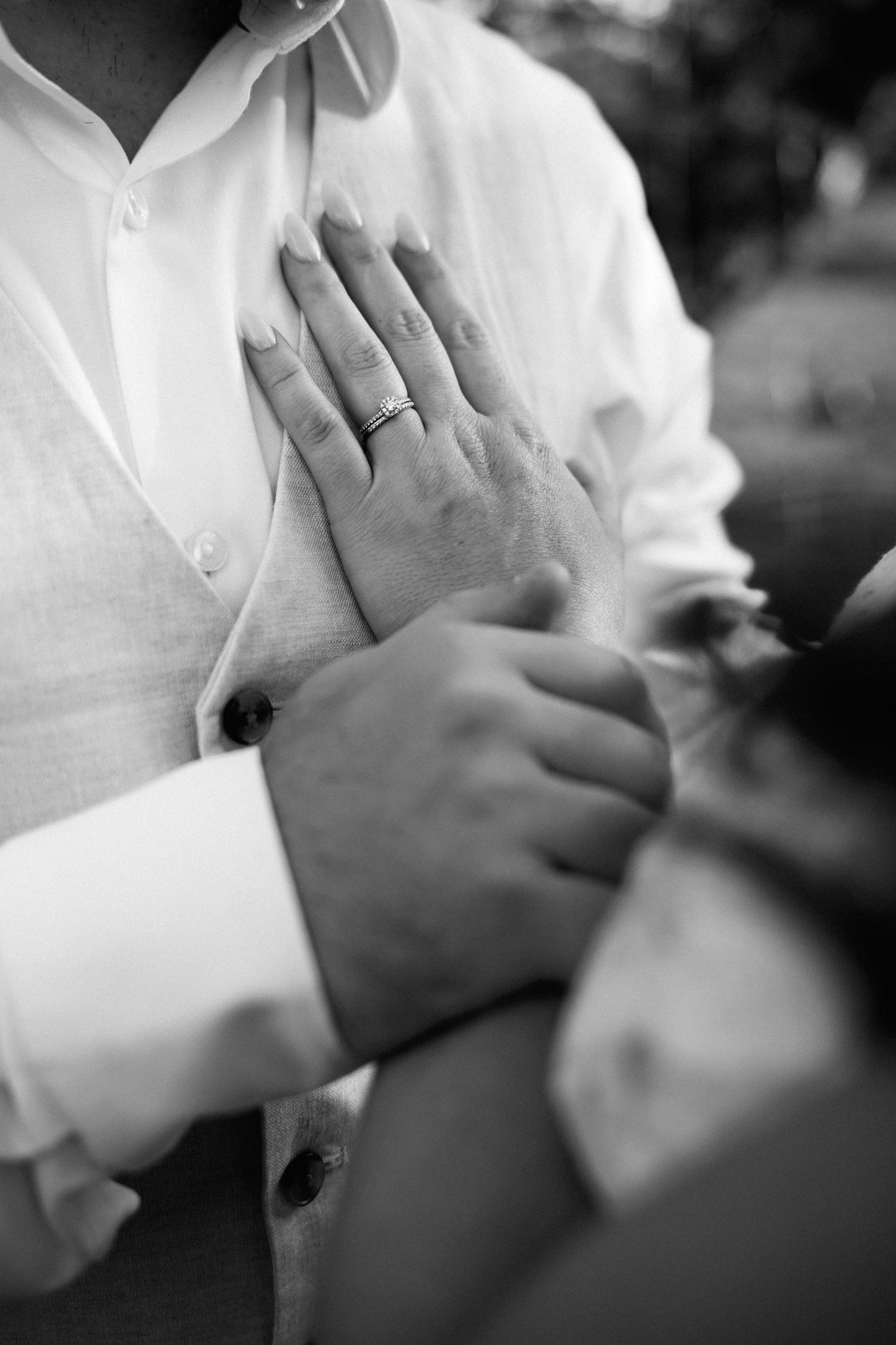 Black and white close-up of bride and groom holding hands, showing wedding ring after ceremony.